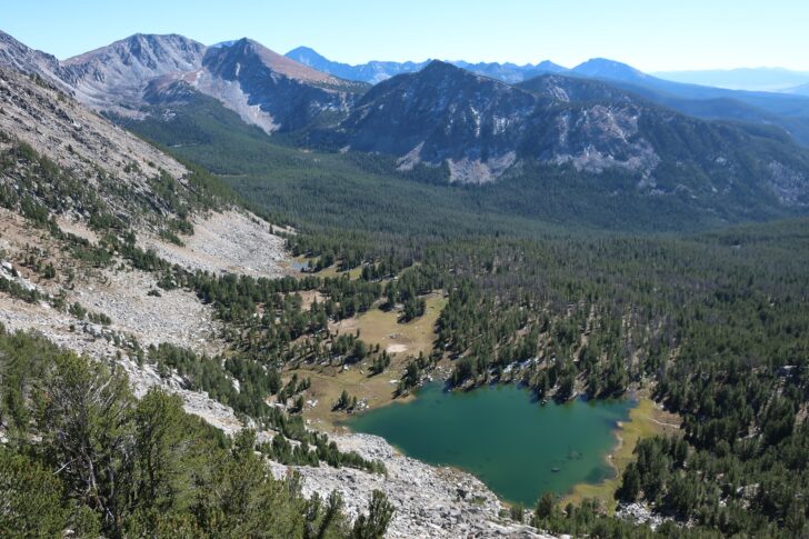 一张以山脉为背景的广角风景照片。在前景中，在山谷中，一个蓝色的湖泊就像绿色森林中的宝石。