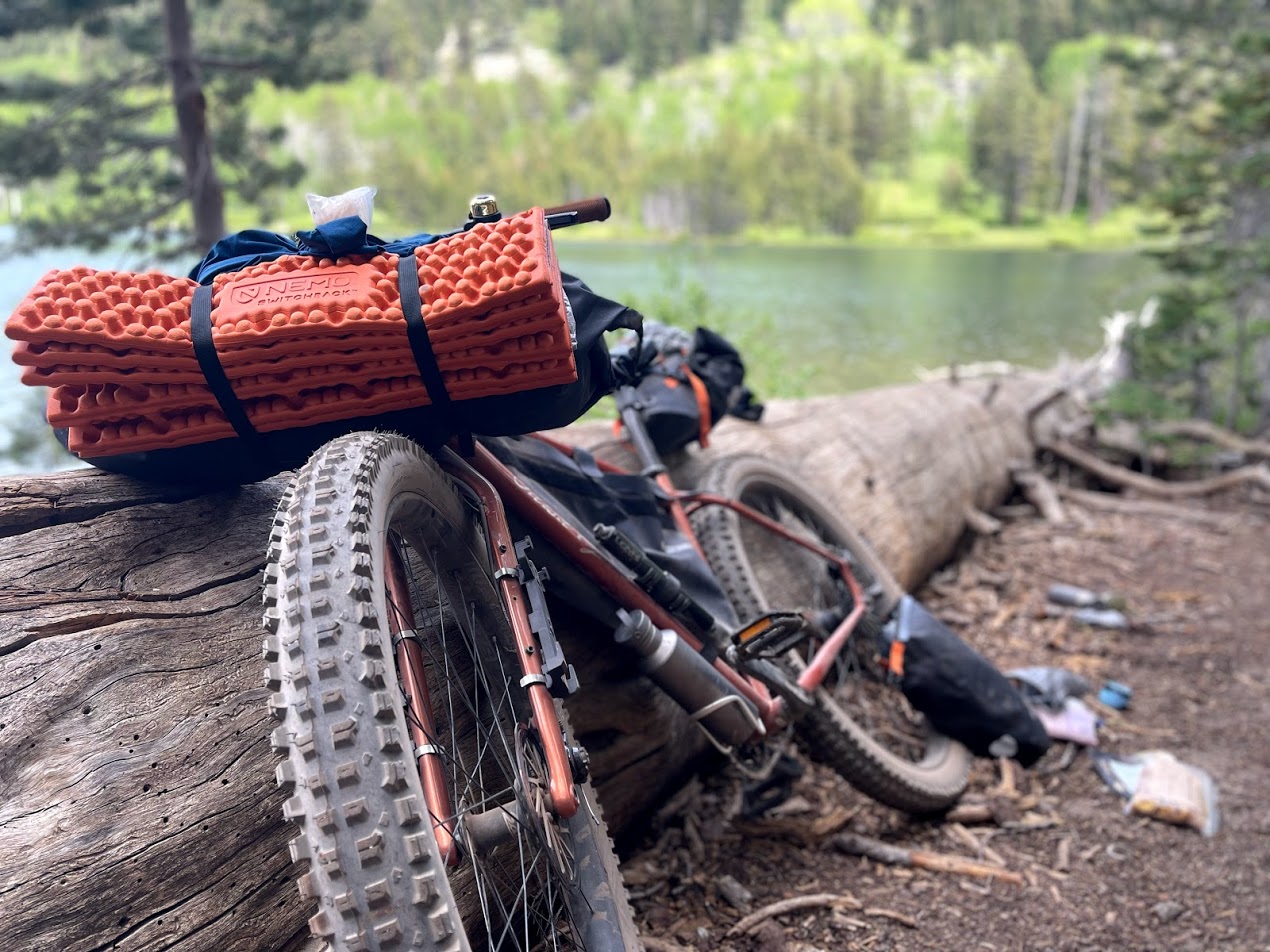 一辆装有自行车的自行车靠在高山湖旁的一根圆木上。