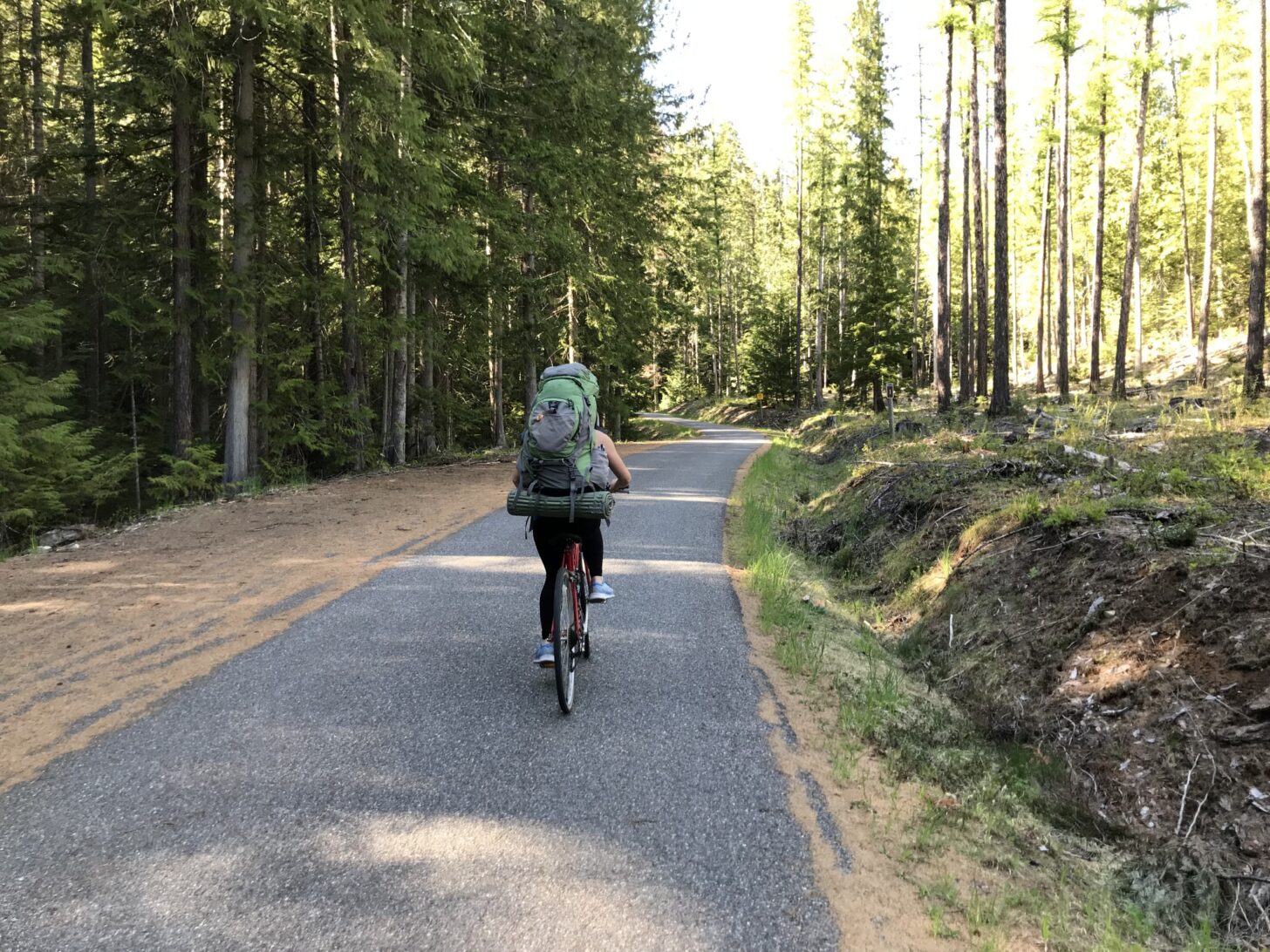 一名女子背着双肩包，骑着自行车走在铺好的小路上